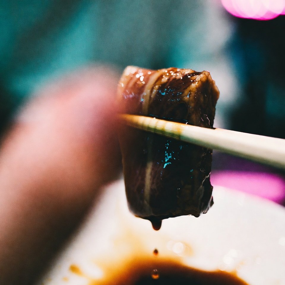 POV chopsticks holding dripping otoro, blurry thumb in frame