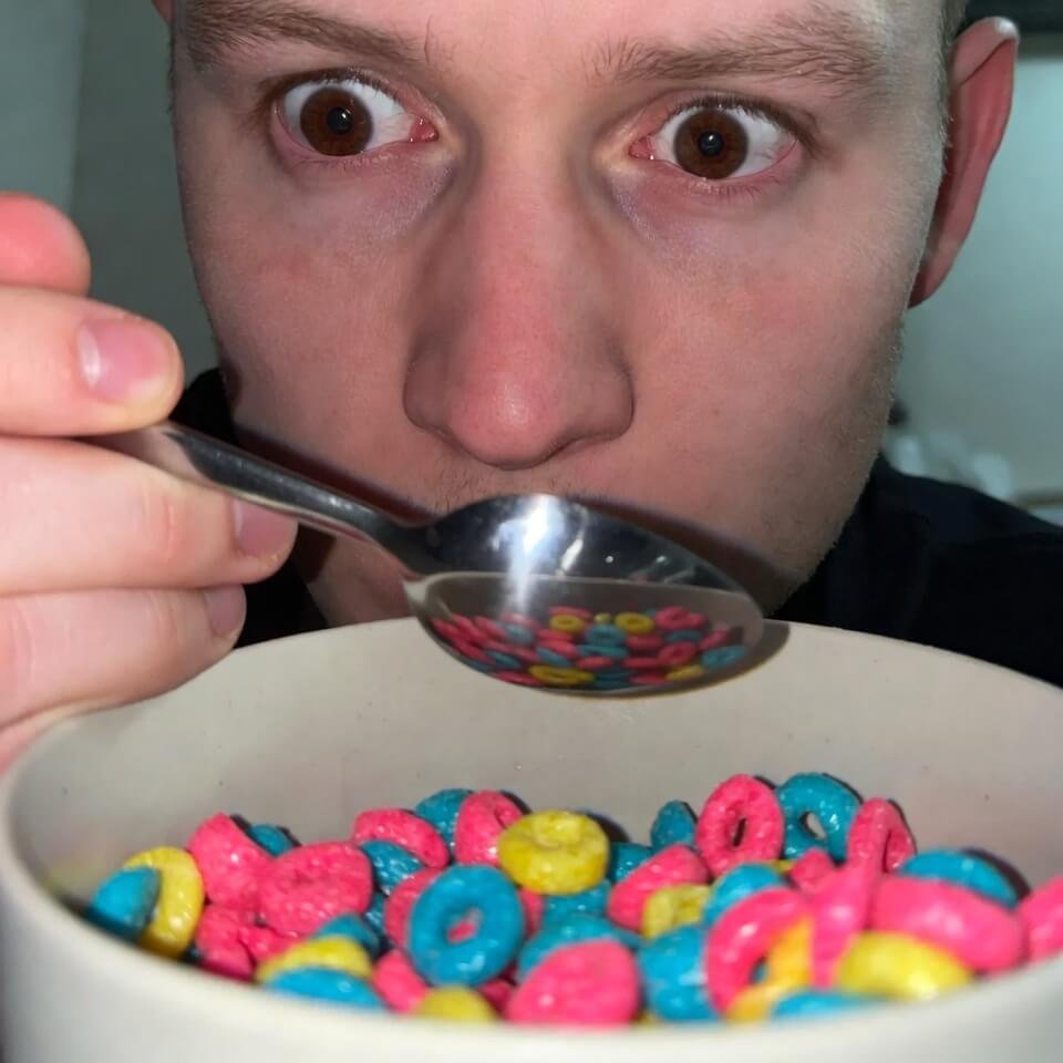Washed-out neon cereal bowl with annoyed face reflected in spoon.